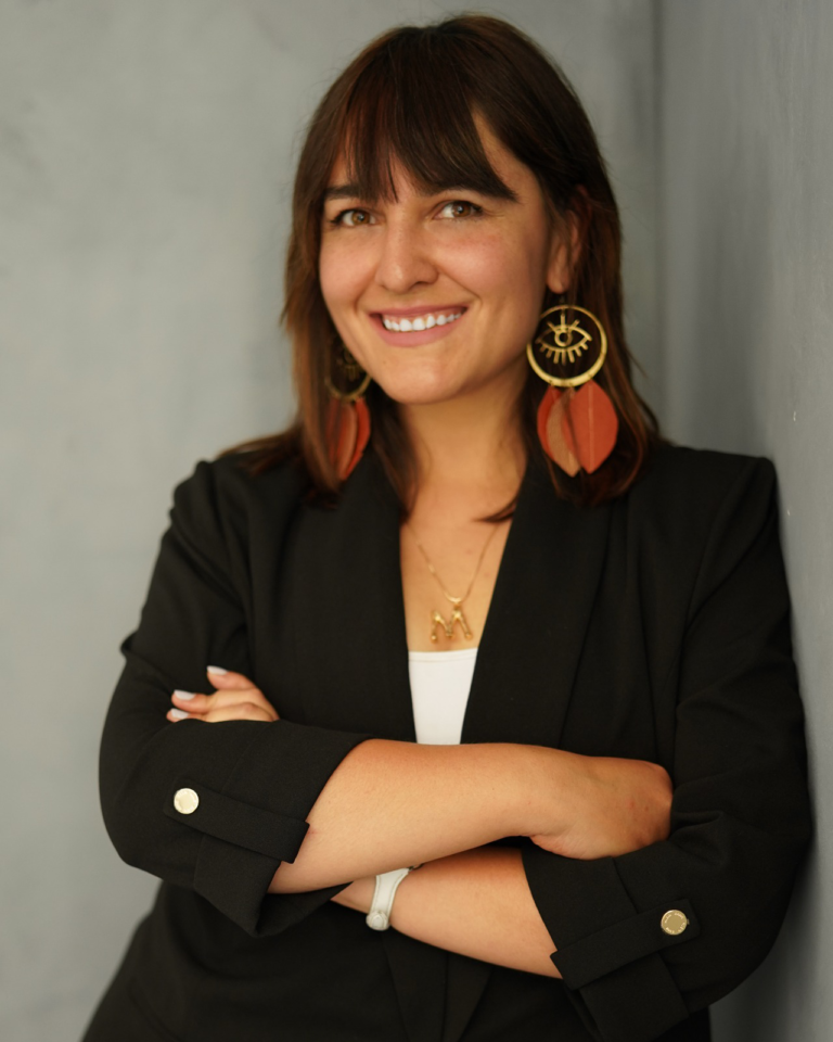 Montserrat Oyanedel Tolmo profile picture posing with a black blazer, large brown earrings and a white undershirt.